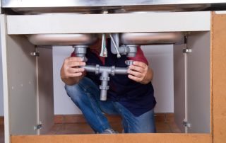 Plumber repairing a clogged garbage disposal under a kitchen sink in Nogales
